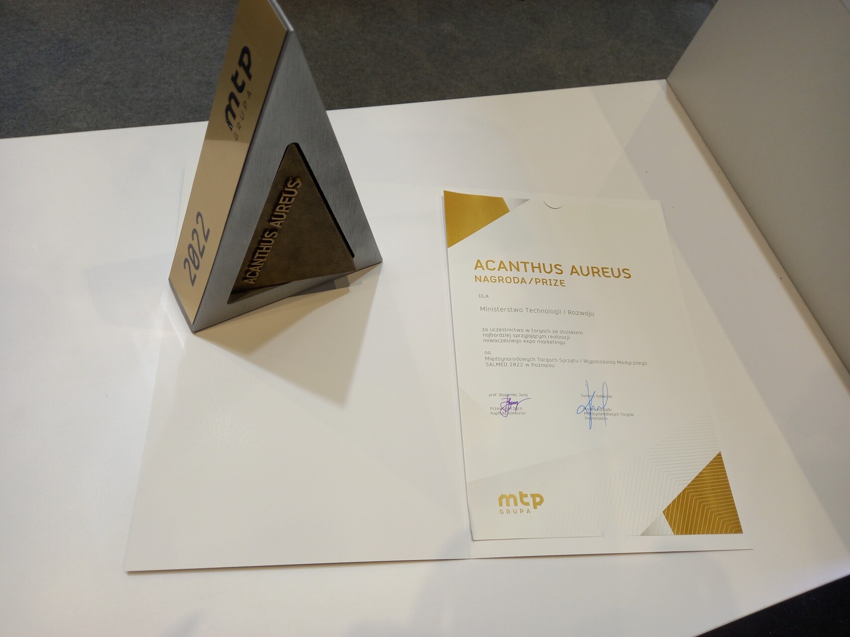 zdjęcie przedstawia kartkę z napisem ACANTUHUS AUREUS oraz statuetkę w kształcie trójkąta z...