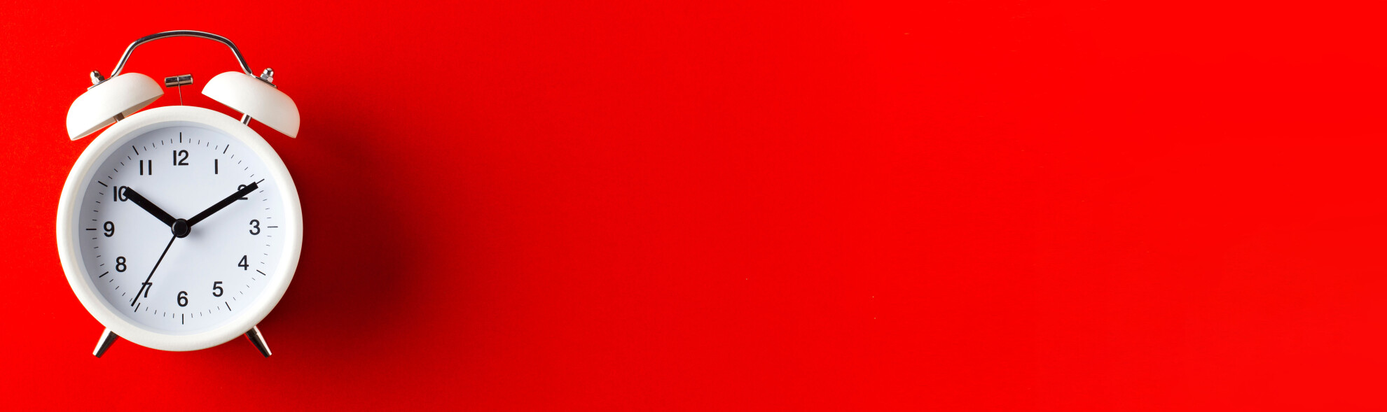 Tradycyjny, stojący budzik na czerwonym tle. 