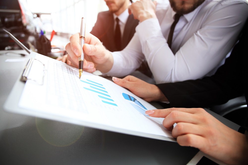 Zbliżenie na ludzi siedzących przy biurku i patrzących się w dokumenty z wykresami