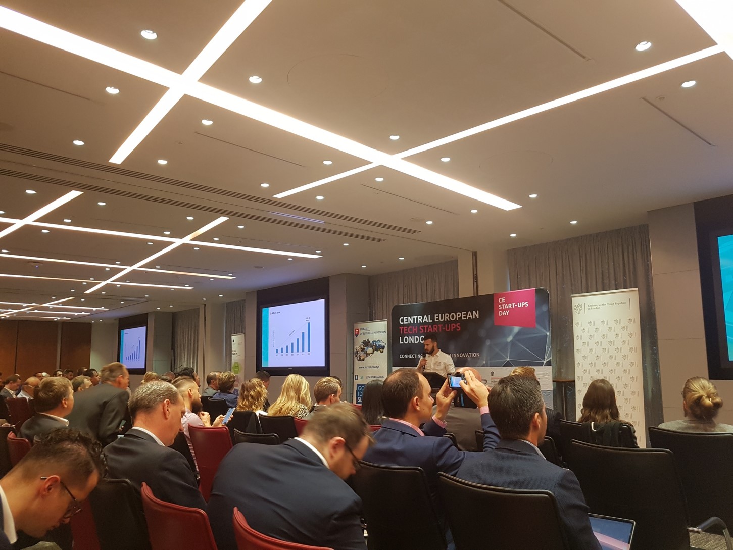 ludzie w różnym wieku siedzą na sali a przed nimi stoi mężczyzna z mikrofonem w ręku