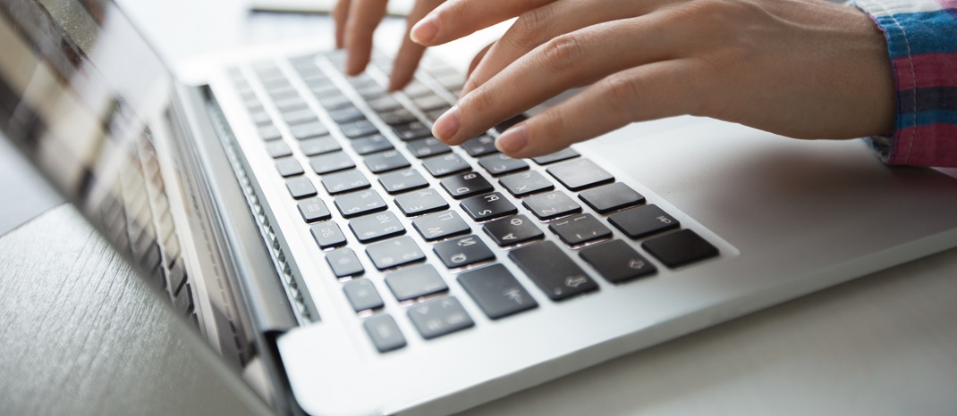 Zbliżenie na klawiaturę laptopa, widać dłonie kobiety, która pracuje na tym laptopie.