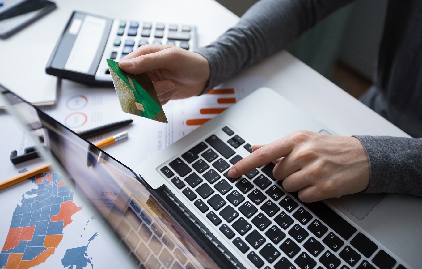 Zbliżenie na ludzką dłoń trzymającą kartę kredytową przy klawiaturze laptopa. 