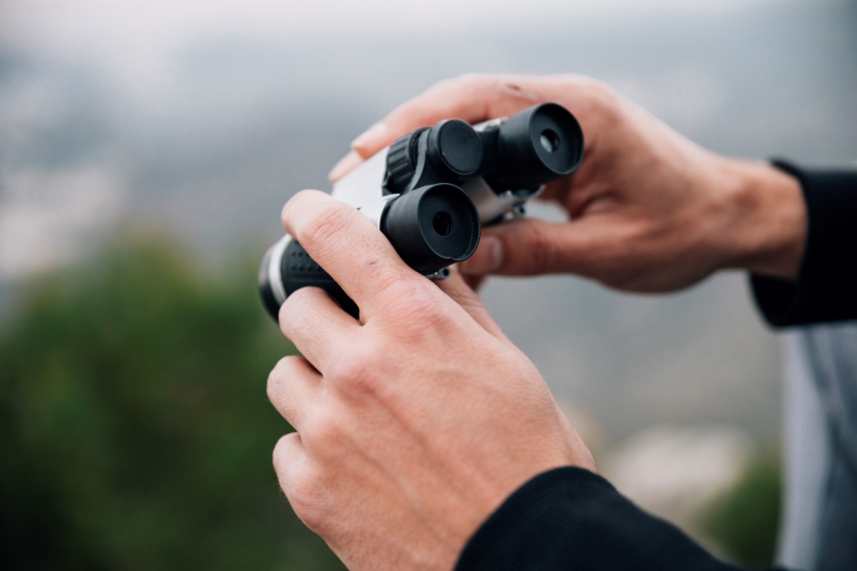 Na zdjęciu mężczyzna trzyma w rękach lornetkę, widać jedynie jego dłonie. tło zdjęcia jest...