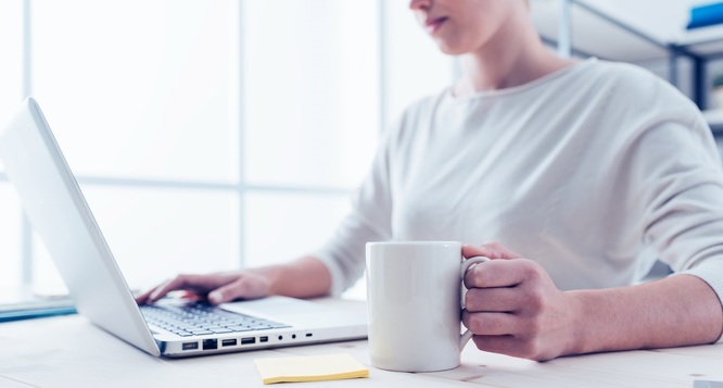 kobieta siedzi przy biurku z laptopem i trzyma kubek za uchwyt