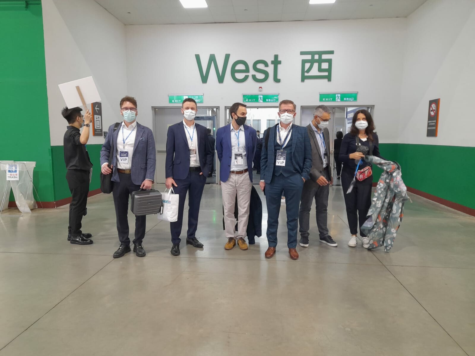 widok na grupę ludzi stojących w holu, ubranych w maski