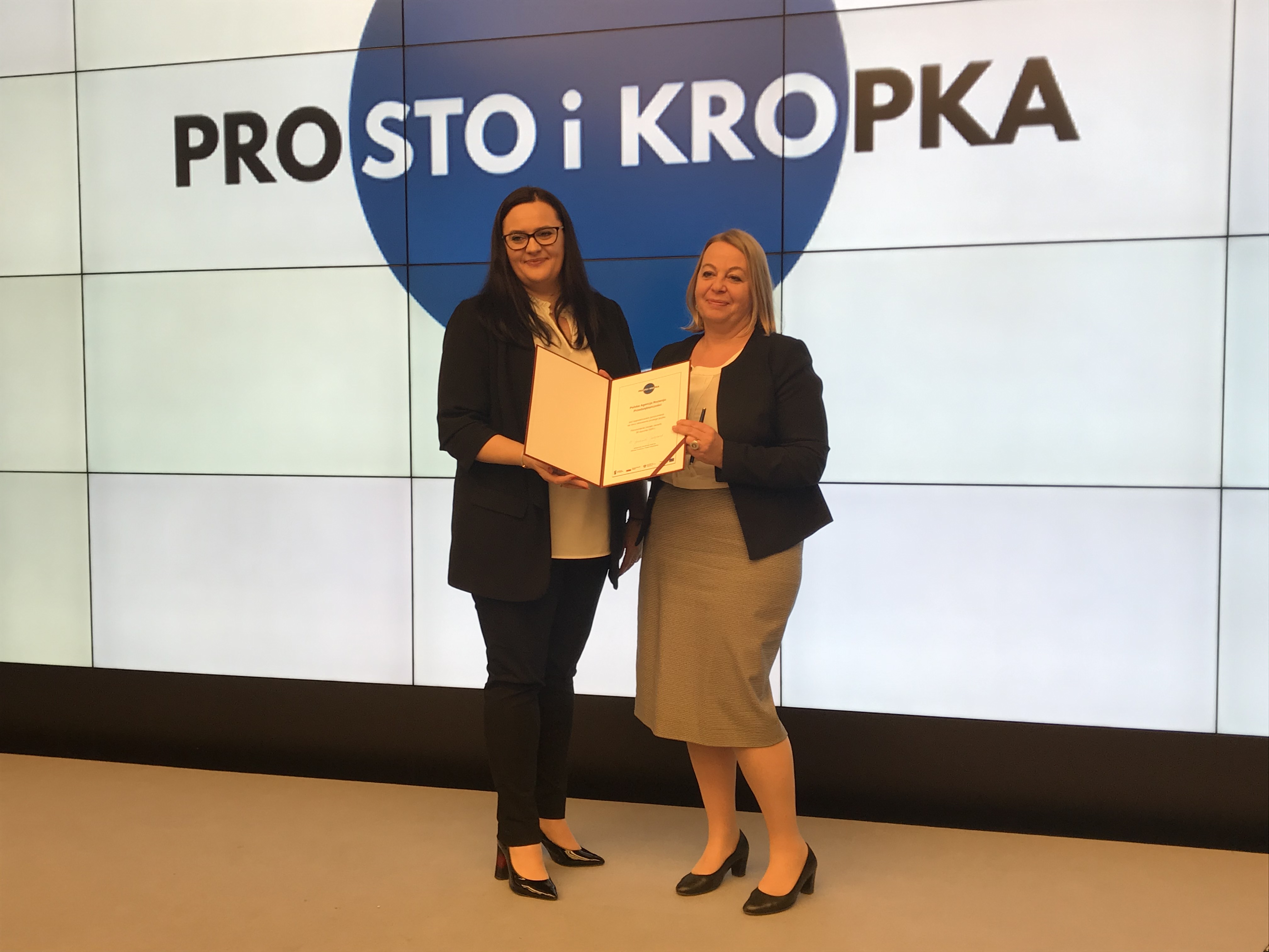 Prezes PARP Małogrzata Oleszczuk stojąca na scenie i wspólnie trzymająca deklarację współpracy na rzecz prostej komunikacji z Minister Funduszy i Polityki Regionalnej Małgorzatą Jarosińską-Jedynak Prezes PARP Małogrzata Oleszczuk stojąca na scenie i wspólnie trzymająca deklarację współpracy na rzecz prostej komunikacji z Minister Funduszy i Polityki Regionalnej Małgorzatą Jarosińską-Jedynak