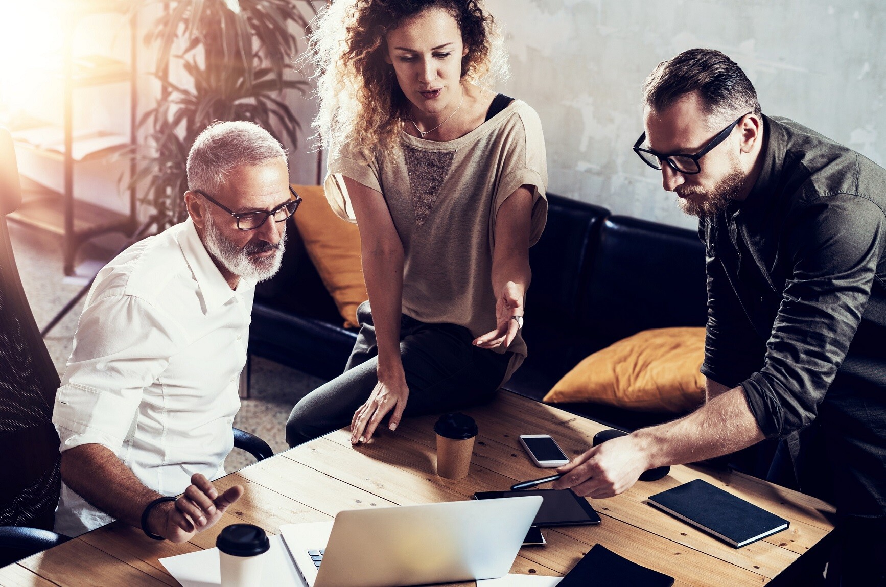 Dwóch mężczyzn i kobieta siedzą przy stole i patrzą się w ekran laptopa