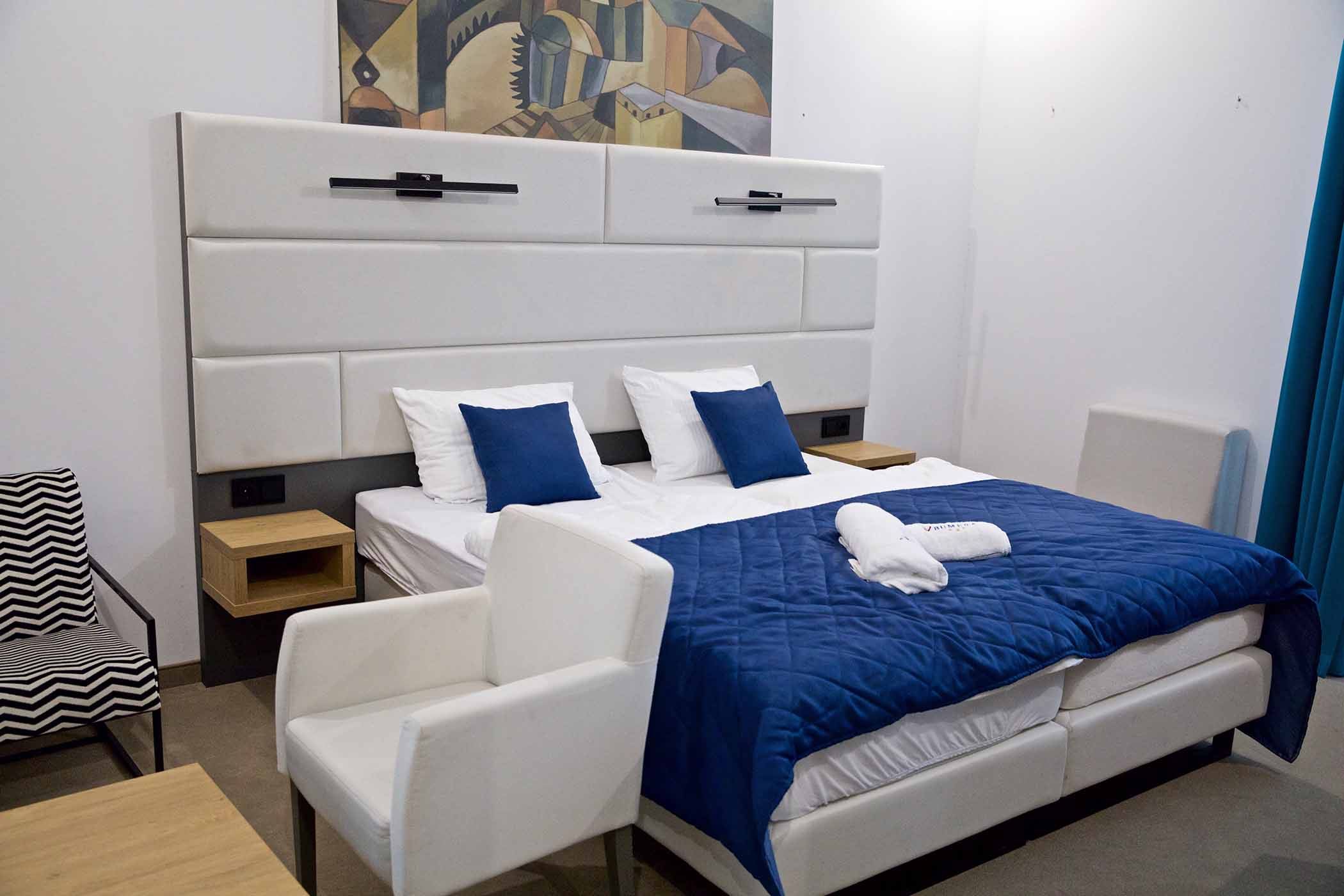 Widok pokoju z meblami jak granatowe krzesło, łóżko z białym zagłówkiem, drzwi ze zdobioną ościeżnicą