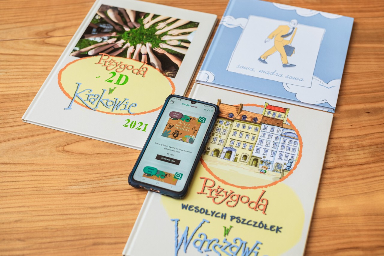 Trzy katalogi leżą na blocie, na nich telefon komórkowy