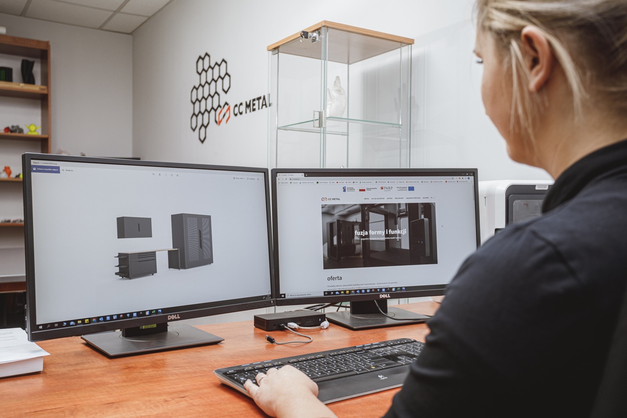 Kobieta siedzi przed dwoma ekranami od komputerów