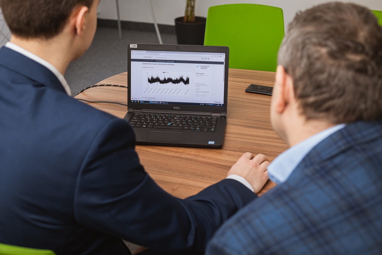 LAptop na stole, przed nim dwóch mężczyzn